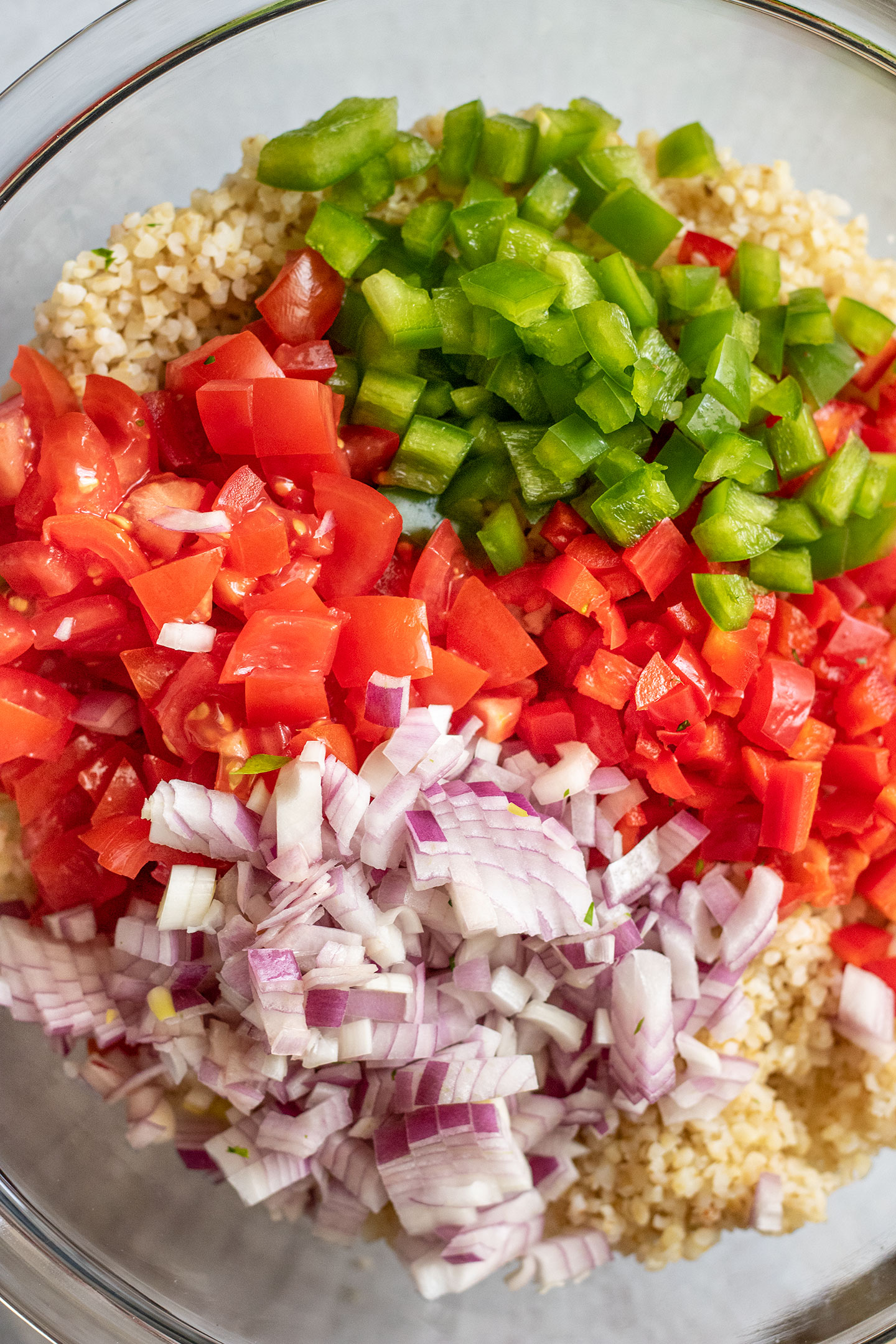 Bowl of bulgur wheat topped with diced peppers, onions, and tomatoes.