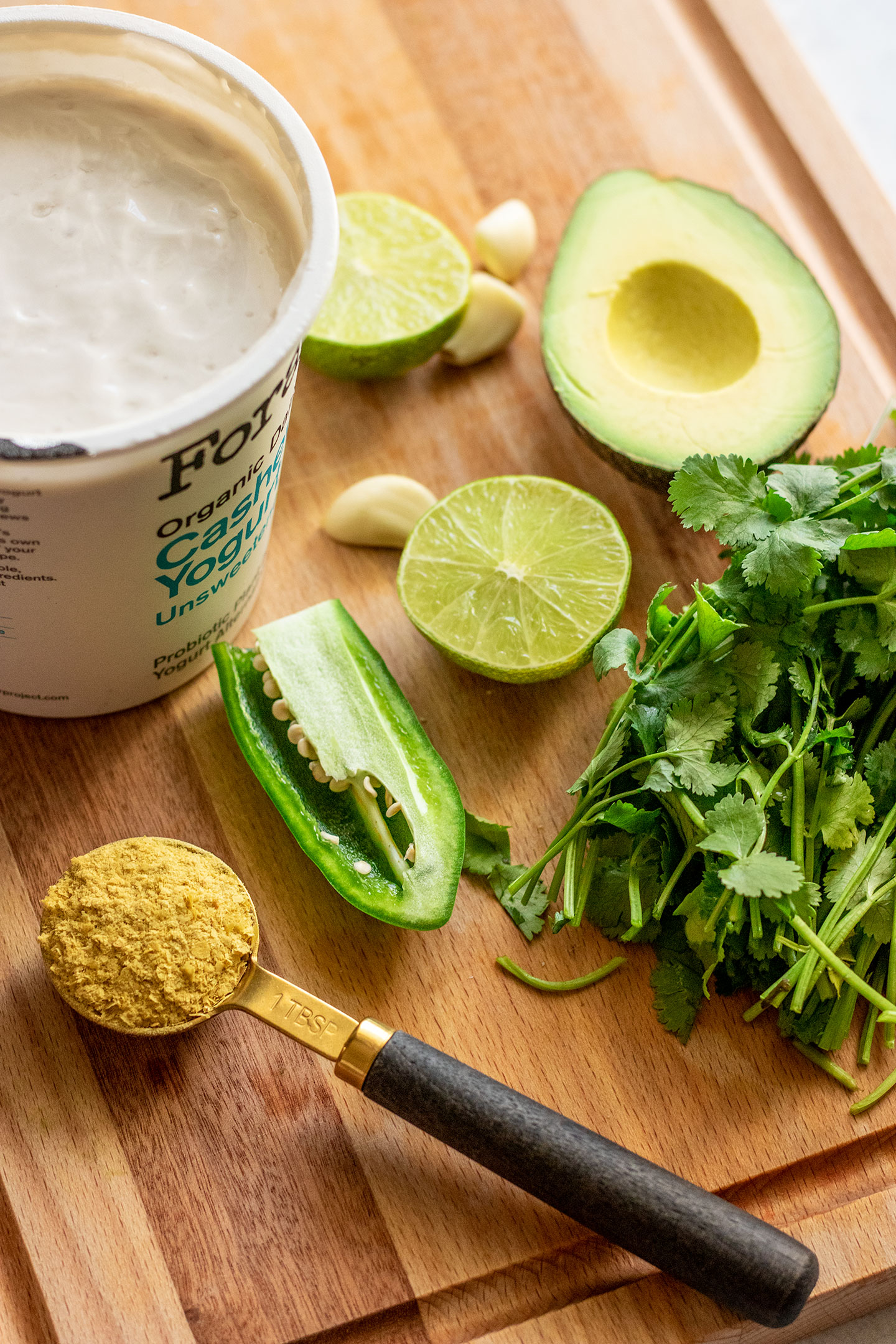 Vegan yogurt, avocado, cilantro, jalapeno, nutritional yeast, and garlic on a cutting board.