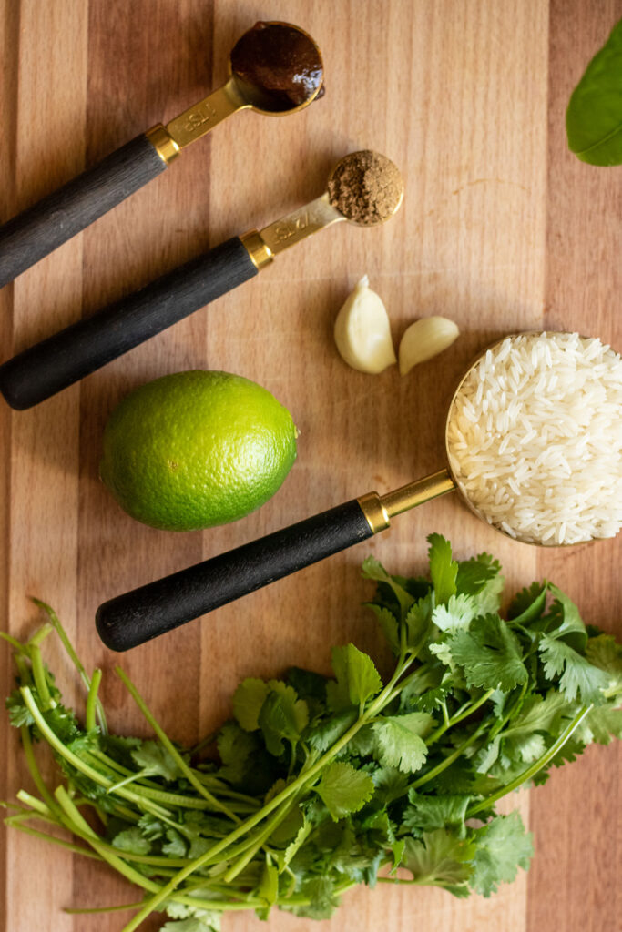 Lime, garlic, rice, cilantro, coriander and vegetable bouillon paste on a cutting board.