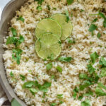 Rice infused with lime juice and cilantro in a pan topped with lime slices and extra cilantro.