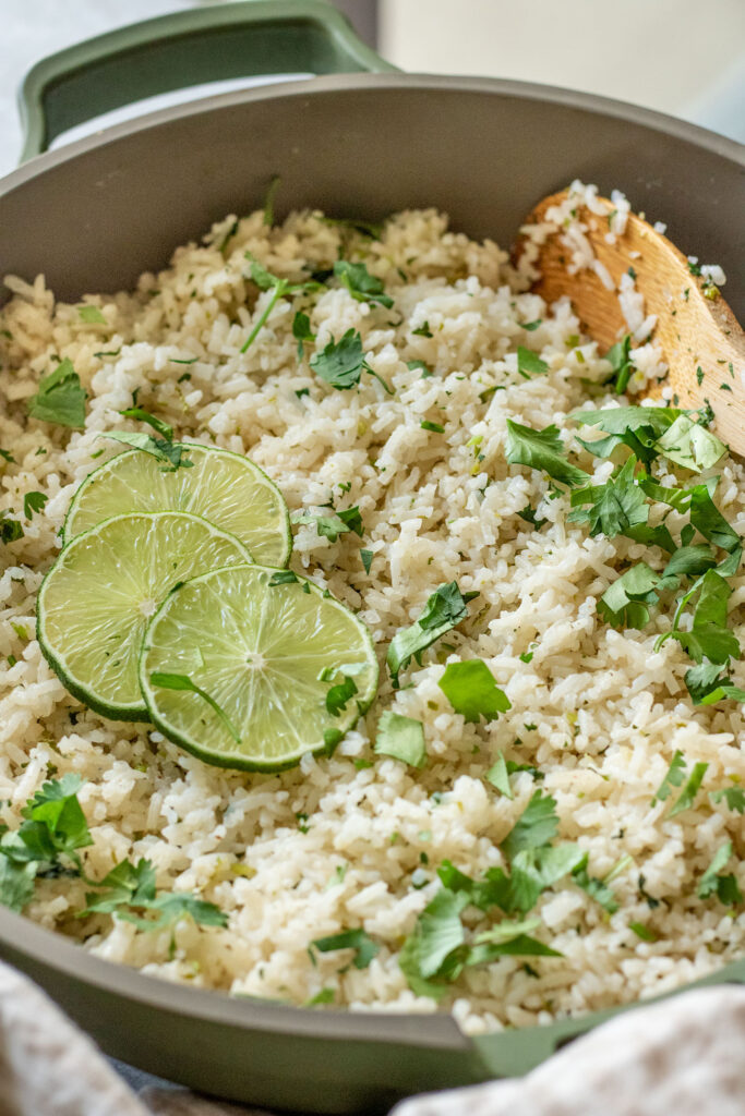Side view of a pan of cilantro lime rice with a spoon tucked in towards the back ready to scoop up some rice.