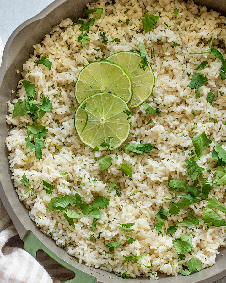 Close up of a pan of cooked cilantro lime rice topped with lime slices and extra fresh cilantro.