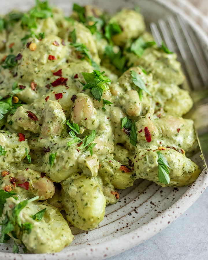 A side view of a plate of creamy pesto gnocchi with a fork tucked in the back.