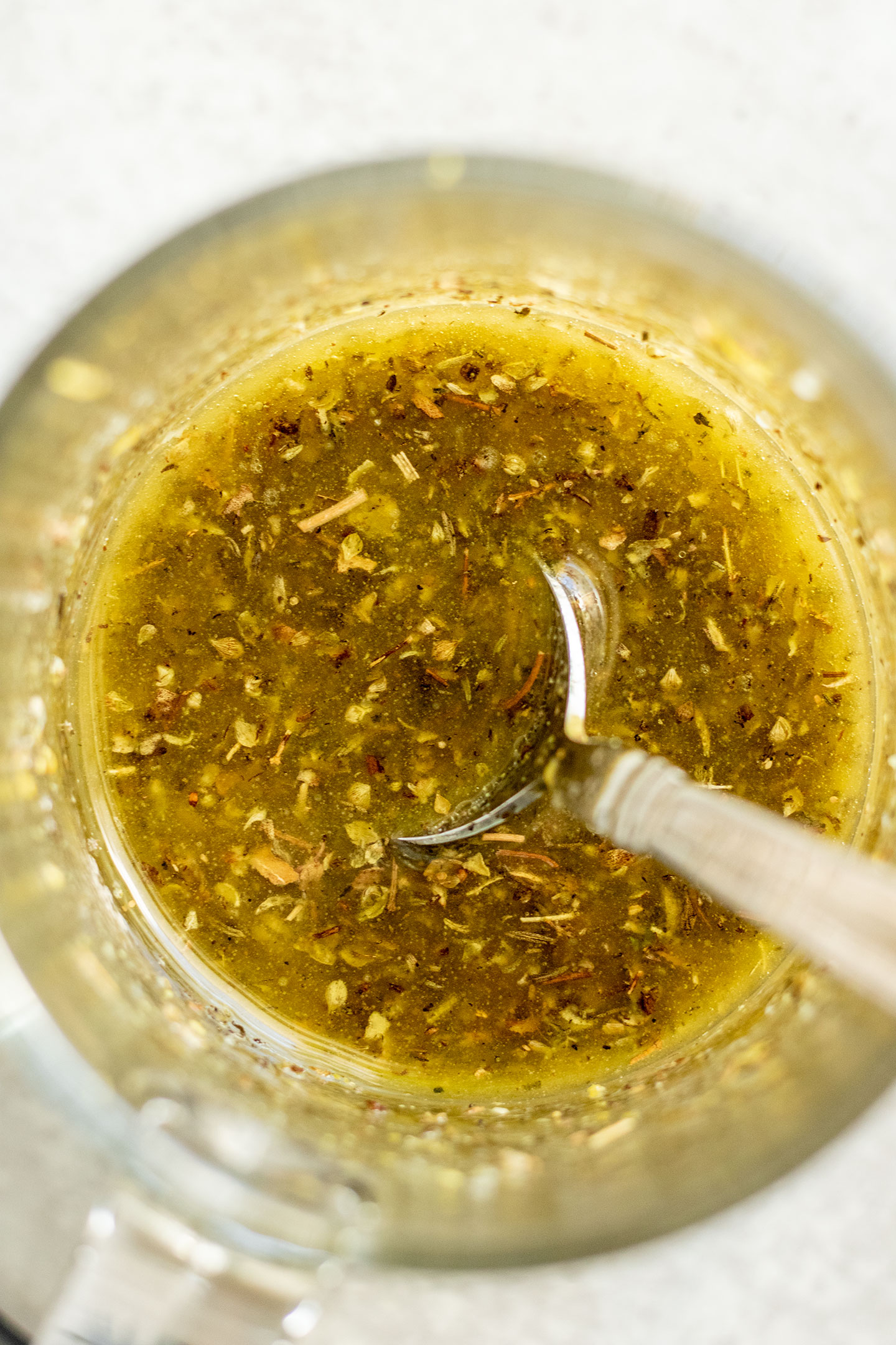 Mixed lemon garlic and herb dressing in a glass with a spoon.