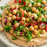 Side view of a plate topped with whole wheat pita smeared with white bean spread and topped with marinated chickpeas.
