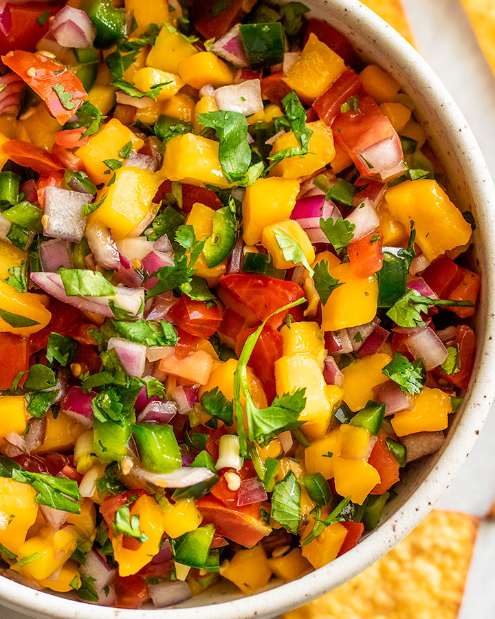 Fully mixed mango salsa served in a white speckled bowl.