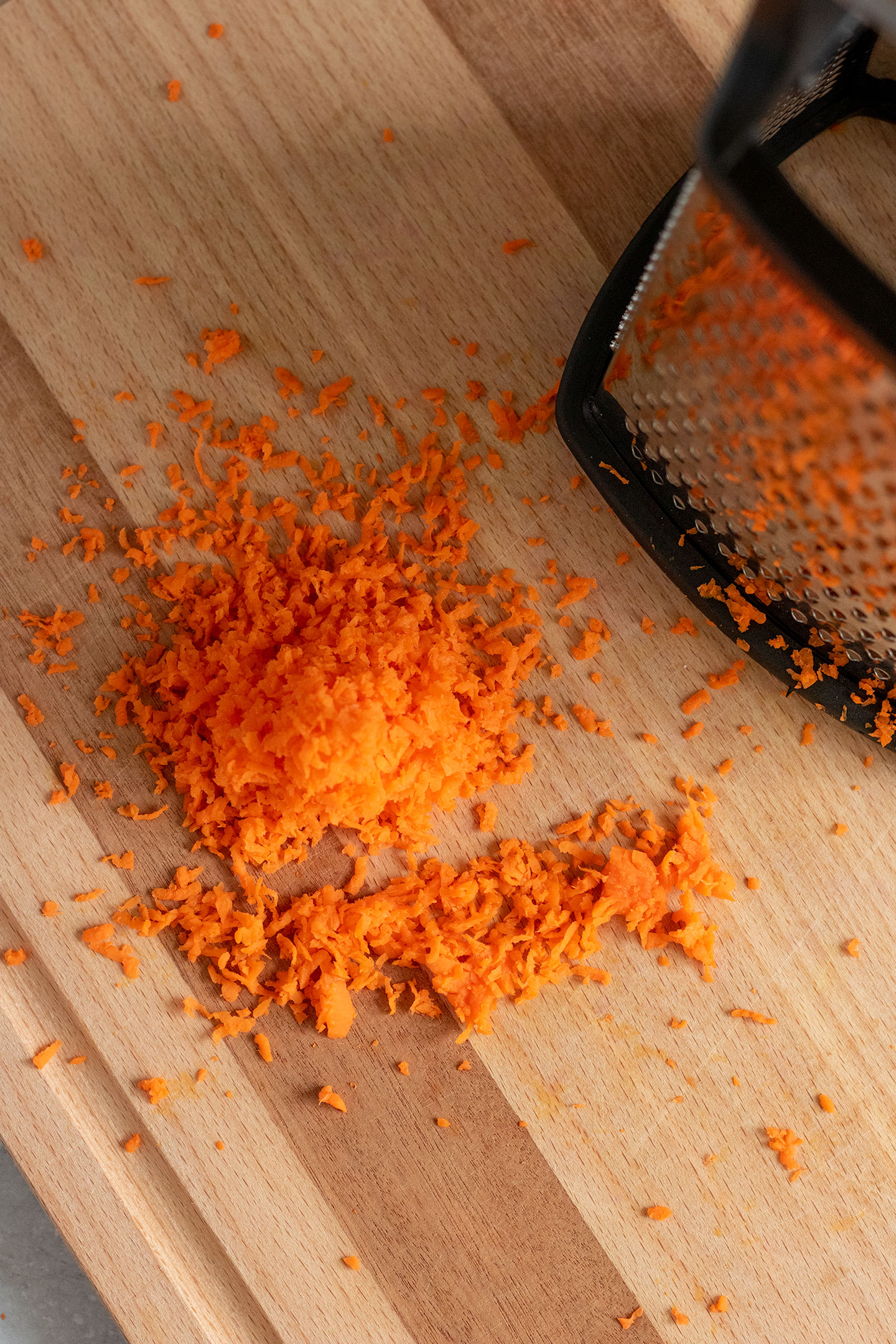 Shredded carrots next to a box grater on a cutting board.