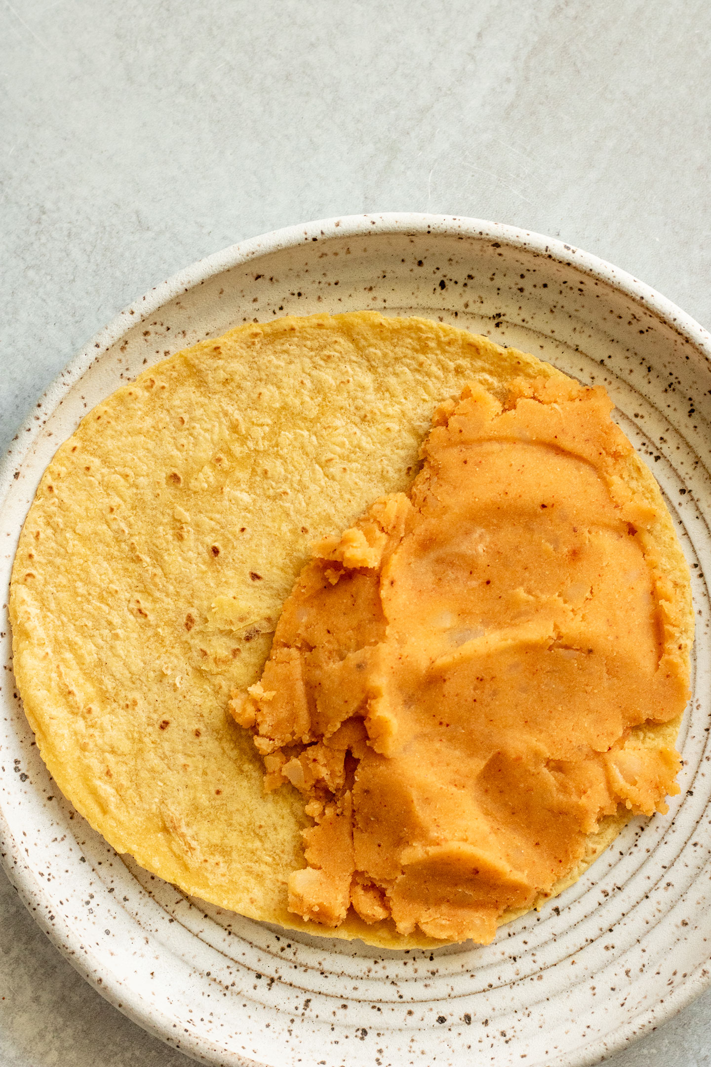 Spreading the seasoned mashed potatoes over half of the warmed yellow corn tortilla.