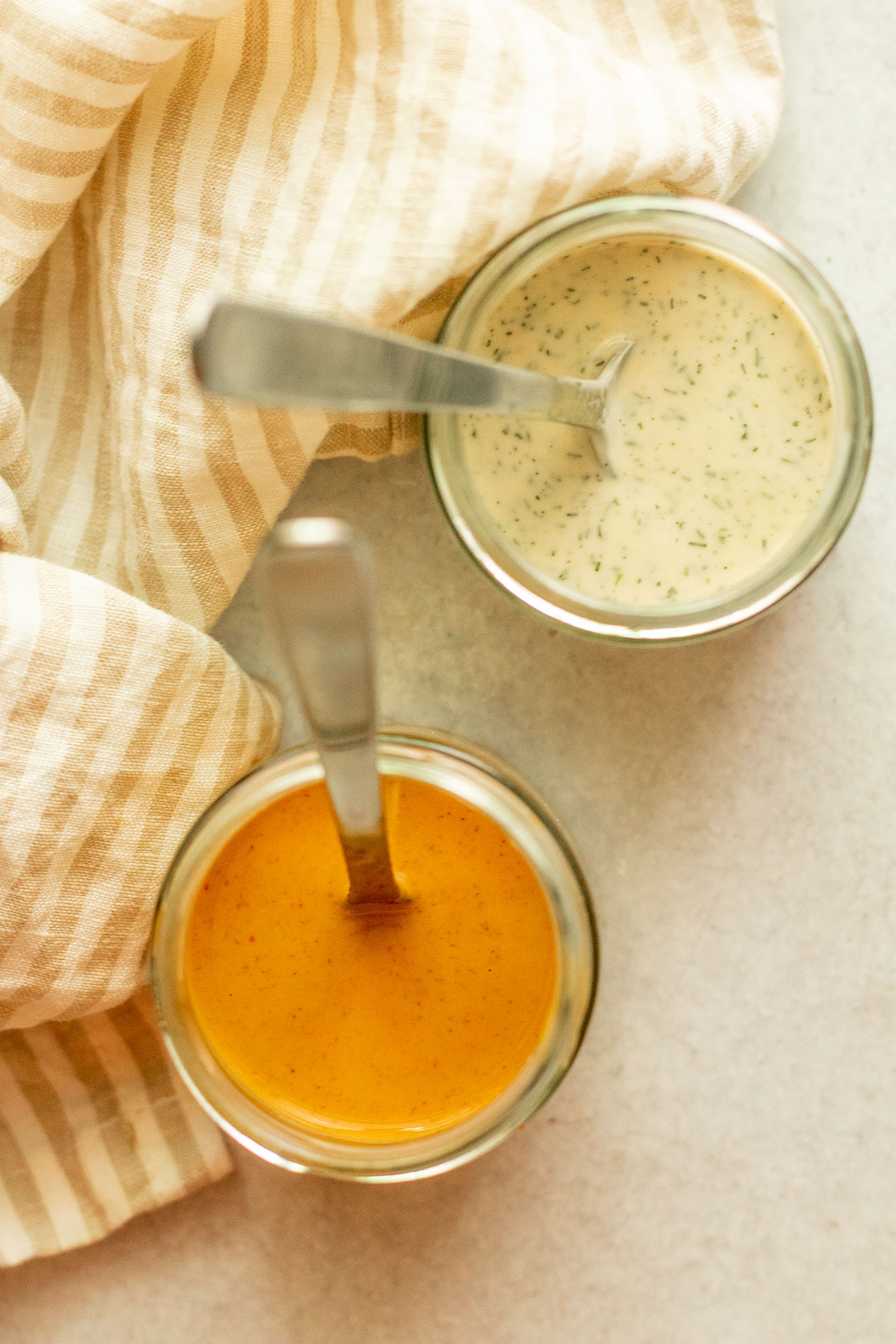 Creamy buffalo sauce and tahini ranch sauce in two separate jars with spoons sticking out of them.