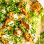 A large close up of a plate of buffalo tofu wraps spread with tahini ranch and topped with lettuce, buffalo tofu and scallions.