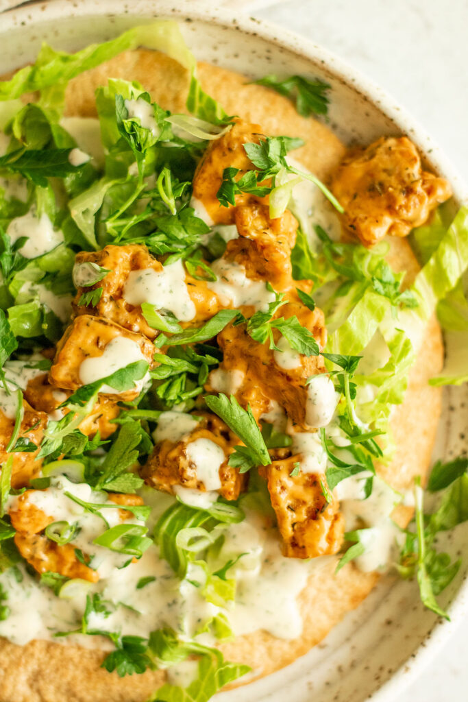 A large close up of a plate of buffalo tofu wraps spread with tahini ranch and topped with lettuce, buffalo tofu and scallions.