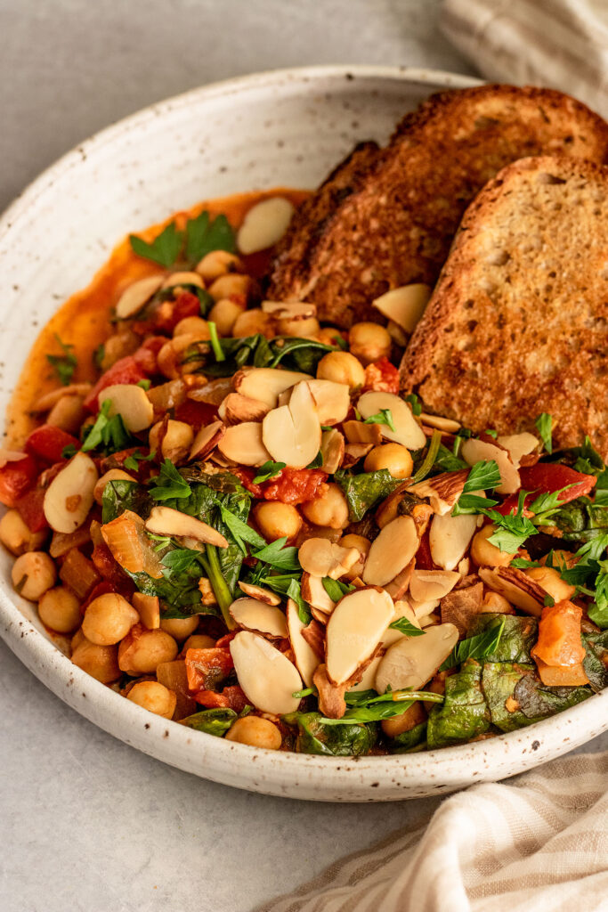 Side view of a bowl of stewed chickpeas served with almonds and toasted bread.