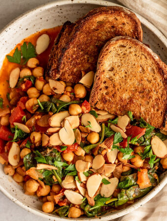 Serving a bowl of stewed chickpeas topped with toasted almonds and crusty bread.