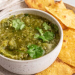 Bowl of freshly made salsa verde with cilantro and freshly baked chips.
