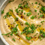 Bowl of white bean dip spread out and drizzled with oil, parsley, red pepper flakes and lemon zest.