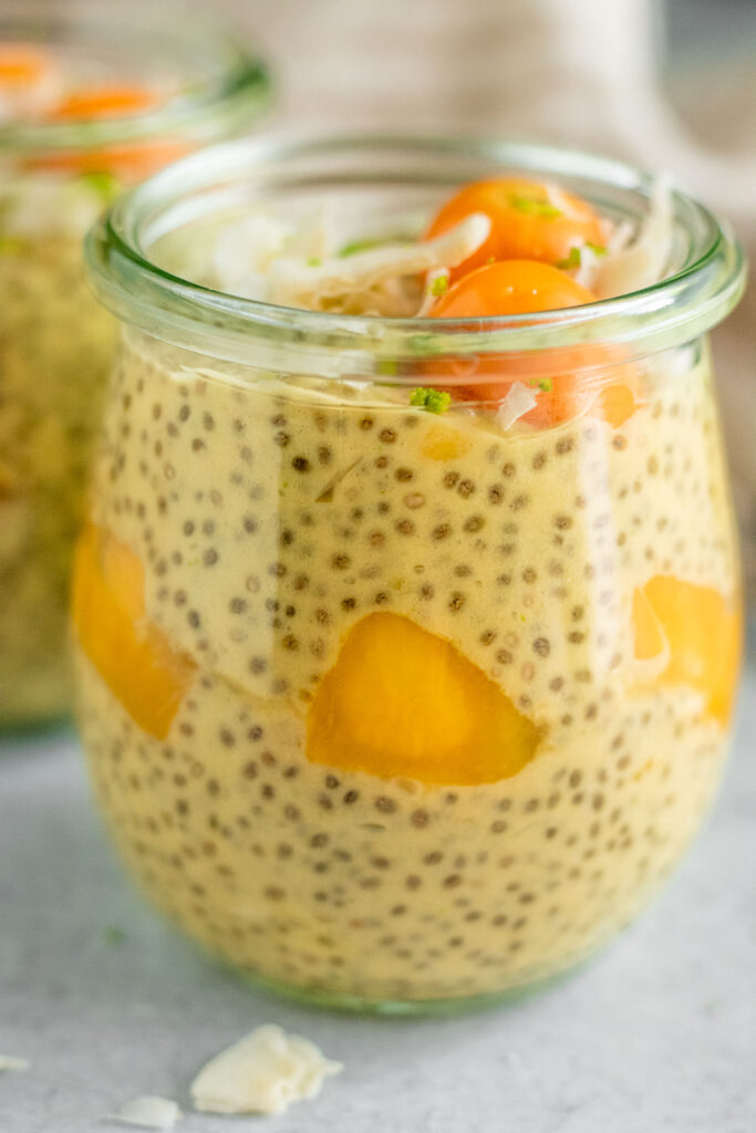 Close up of a large jar of mango chia pudding layered with mango chunks and topped with lime zest and coconut flakes.