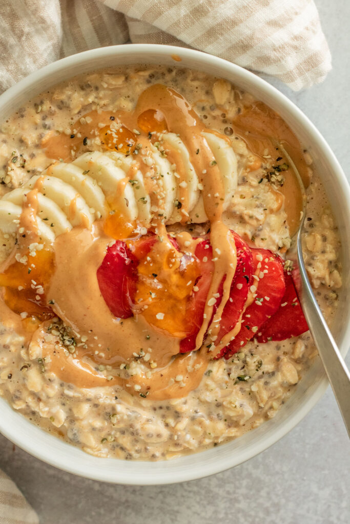 Top down view of a bowl of pb and j oats topped with peanut butter, strawberries, jam, and banana slices with a spoon tucked to the side.