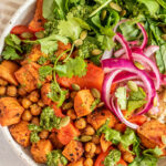Top down view of bowl of roasted chickpeas and sweet potato served with greens, pickled onions and rice.