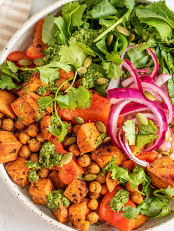 Bowl of chickpeas and sweet potato served with greens, pickled onions and rice.