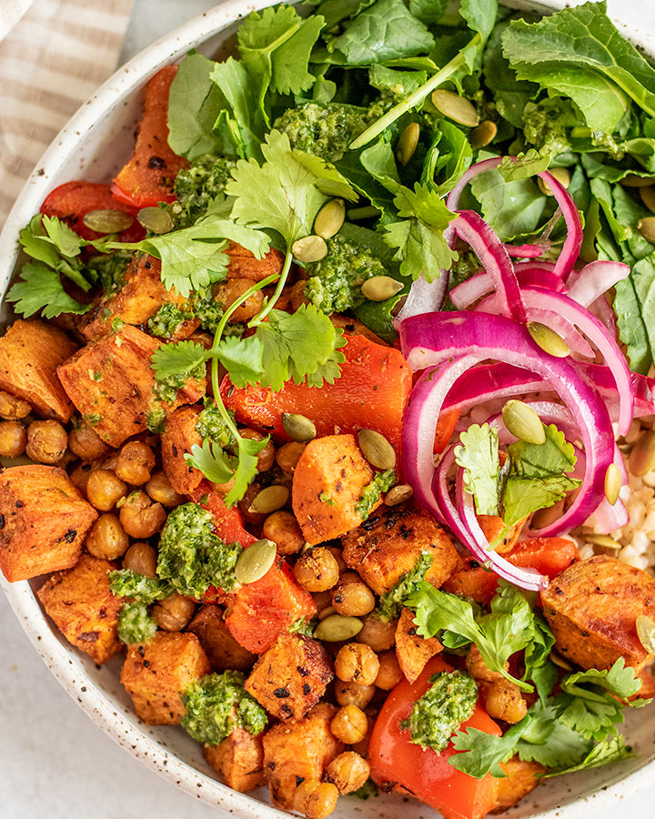 Bowl of chickpeas and sweet potato served with greens, pickled onions and rice.