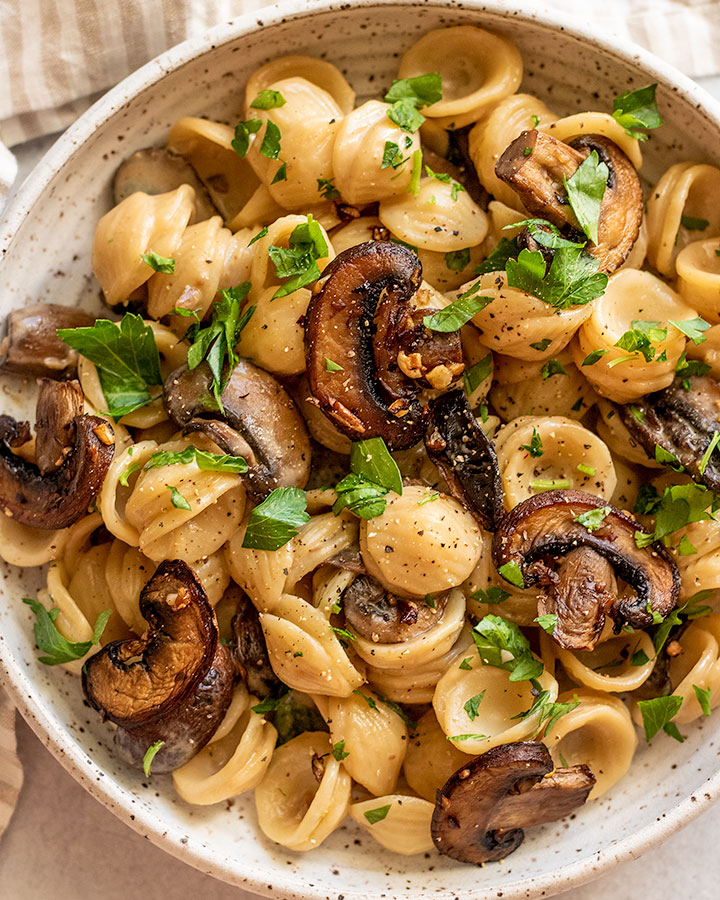 Close up top down view of a white bowl with miso pasta mixed with mushrooms and parsley.