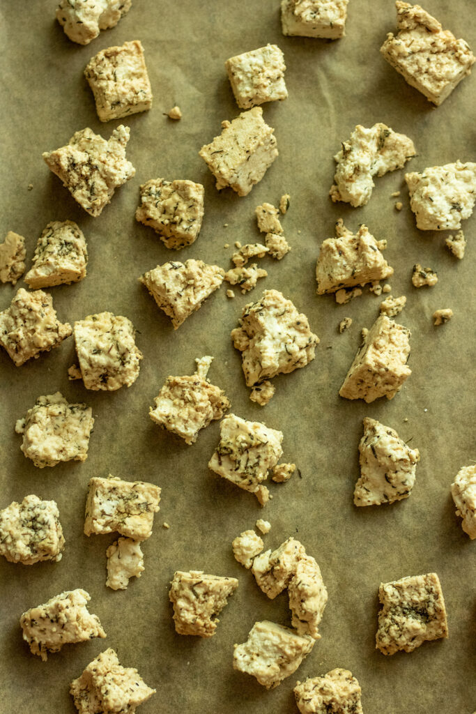 Coated tofu spread out in a single layer on a lined baking tray.