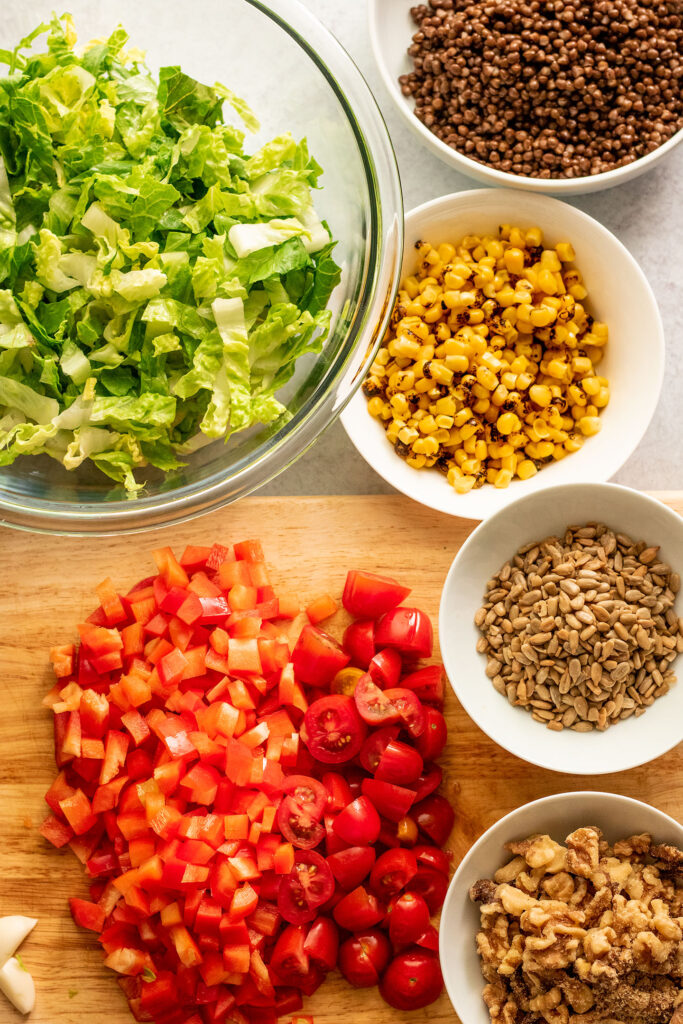 Burrito bowl ingredients including corn, walnuts, sunflower seeds, lettuce, tomatoes, bell pepper and lentils.