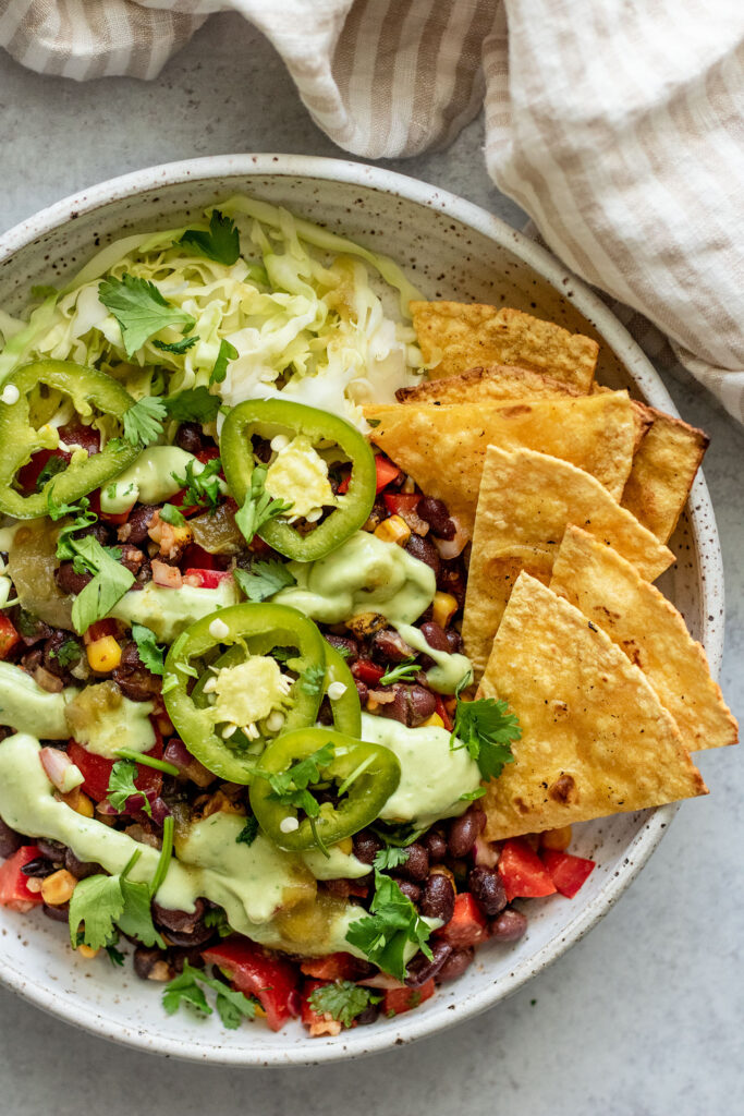 Top down view of a zesty lime marinated black bean bowl topped with pickled jalapeno, cilantro and a creamy cilantro lime sauce and served with chips.