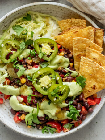 Close up of a bowl of marinated black beans topped with pickled jalapeno, a creamy avocado sauce and served with chips.