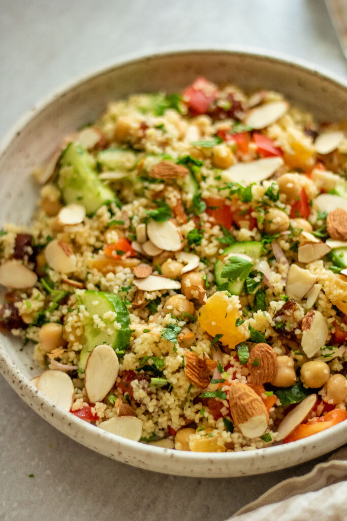 Side view of a mixed citrus infused couscous salad topped with more almond slices and fresh parsley and mint.