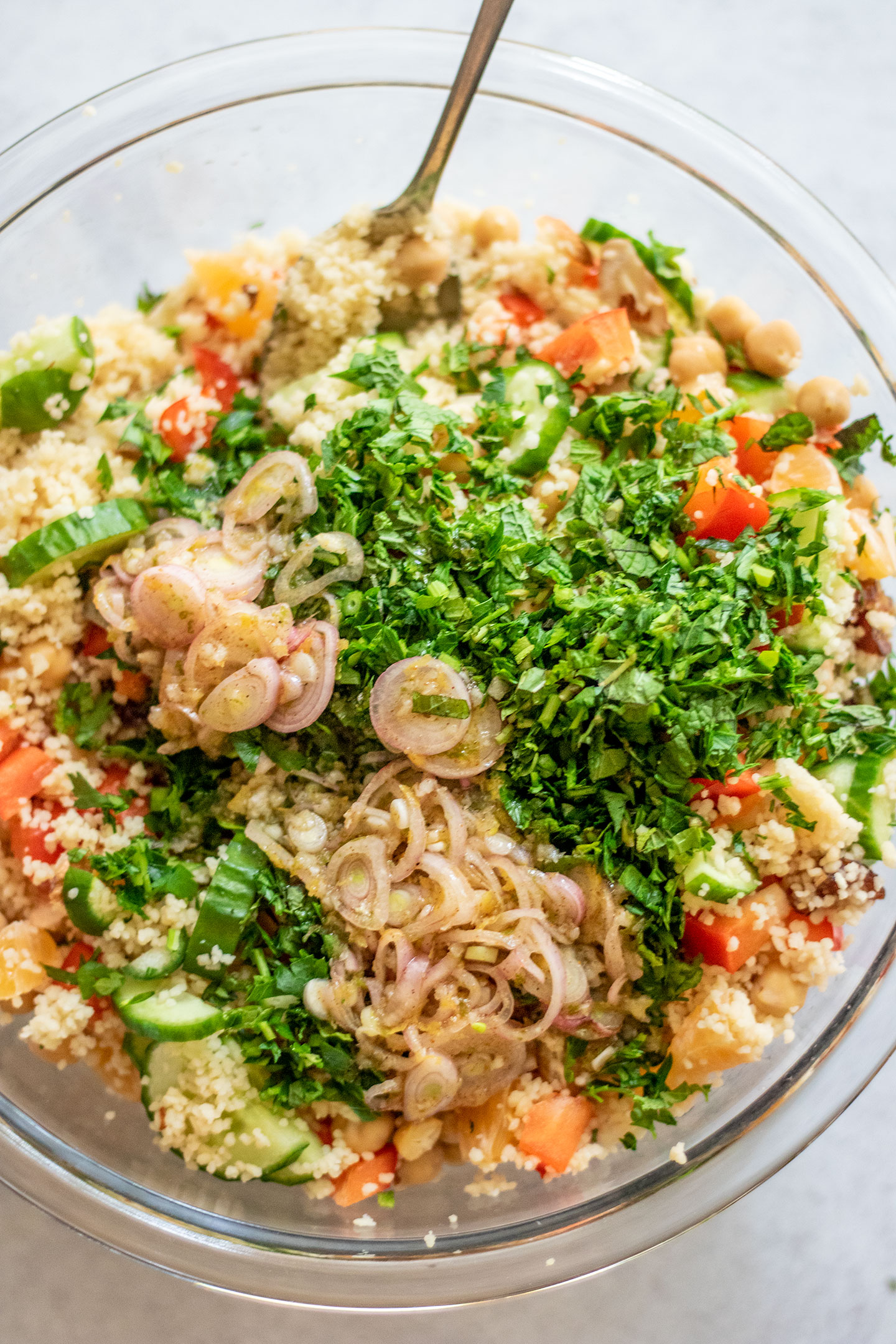 Giant bowl of mixed couscous topped with chopped peppers, cucumbers, chickpeas, dried fruit, oranges, and fresh herbs and dressing in a large glass mixing bowl.