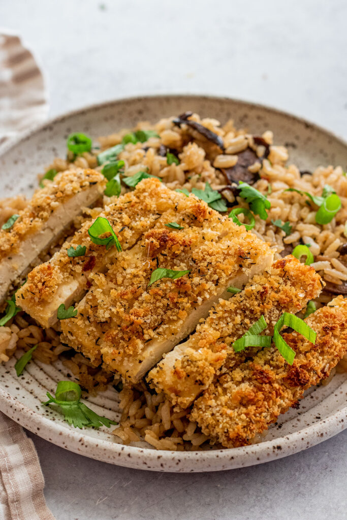 Side view of strips of crispy tofu plated over fried rice.