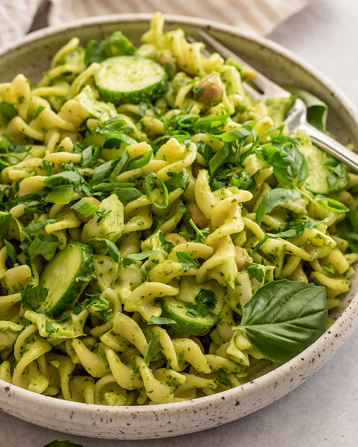 Close up of a bowl of green goddess pasta salad topped with extra scallions and parsley with a fork tucked in the back of the bowl.