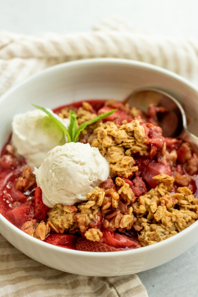 Strawberry crisp with two scoops of ice cream in a bowl and a spoon tucked in the back.