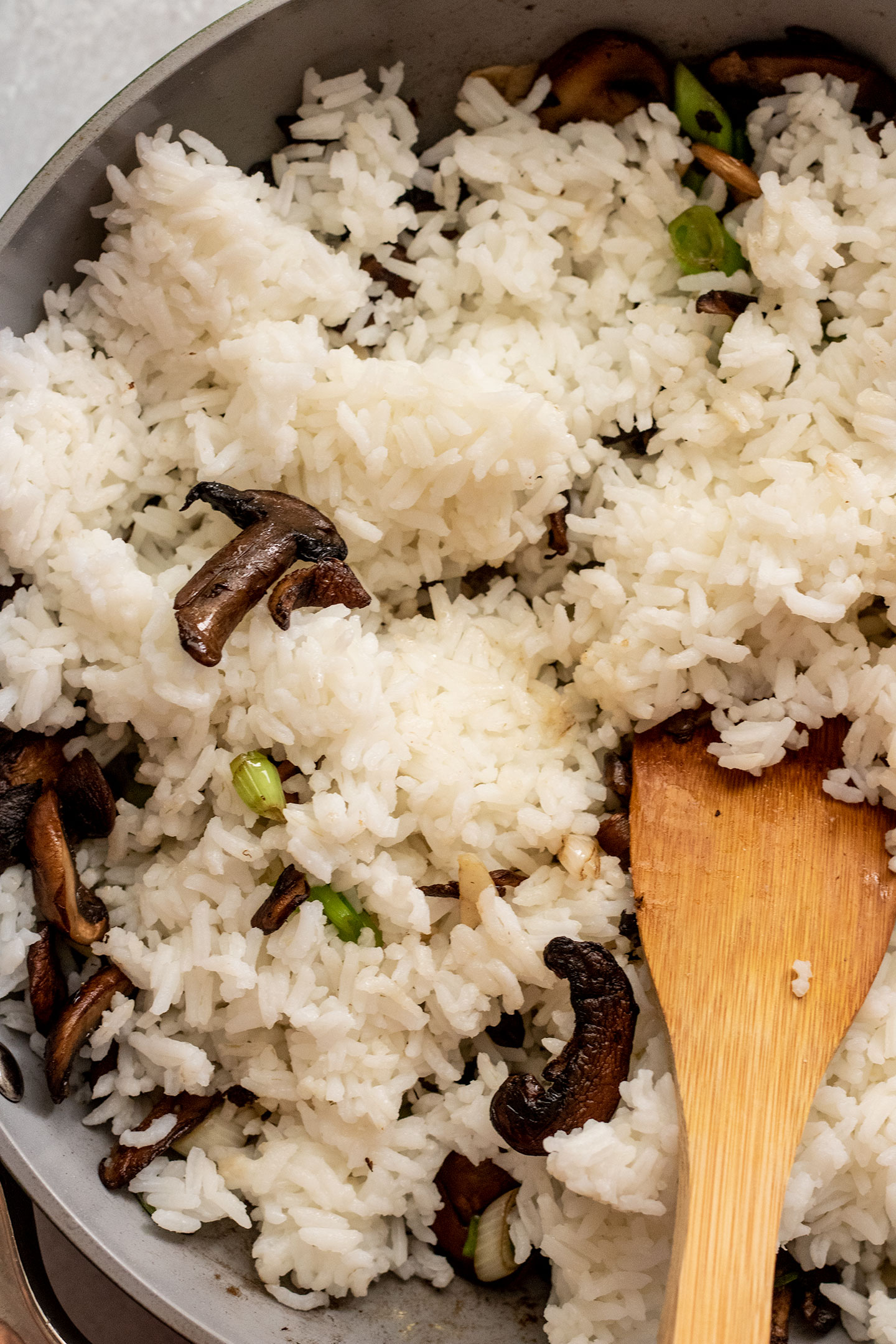 Adding cold rice to a pan of stir-fried mushrooms and scallions.