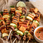 Close up of a pile of tofu skewers and vegetables grilled with extra barbecue sauce on the side.