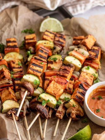 Close up of a pile of tofu skewers and vegetables grilled with extra barbecue sauce on the side.