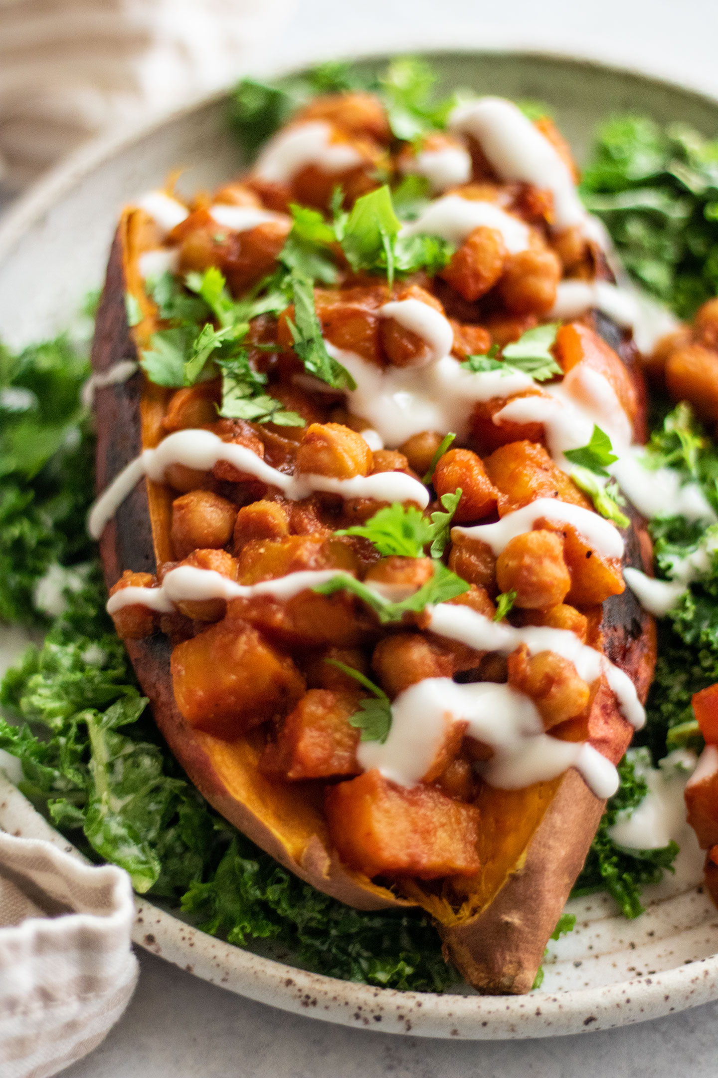 Side view of a large sweet potato loaded with barbecue chickpeas and topped with a creamy yogurt sauce and served over a bed of massaged kale.