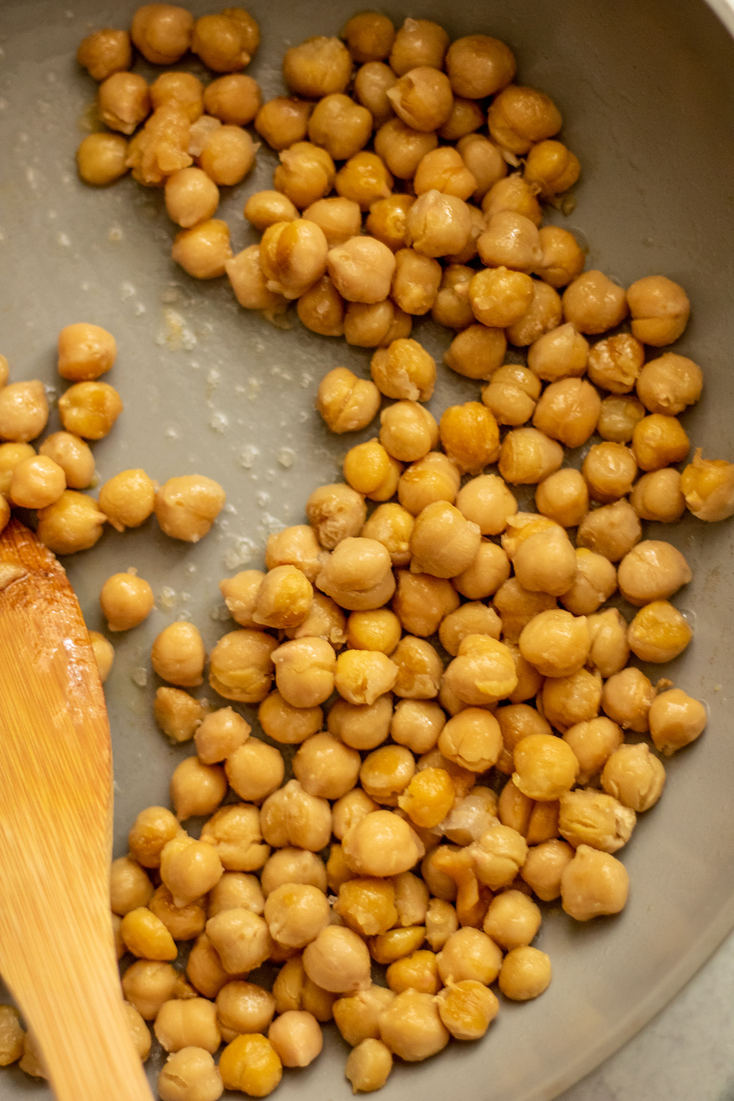 Chickpeas sautéing in oil in a pan.