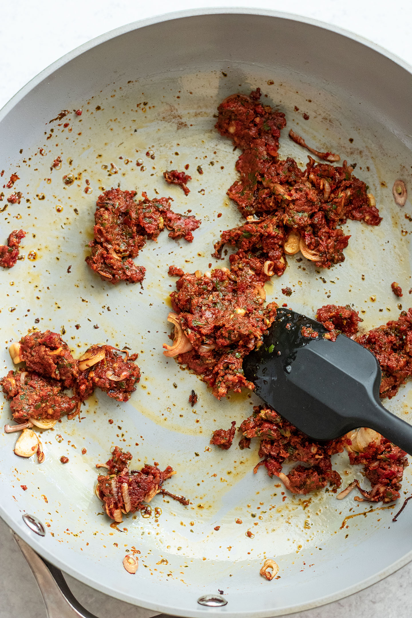 Sautéing red pesto with shallots and garlic in a pan.