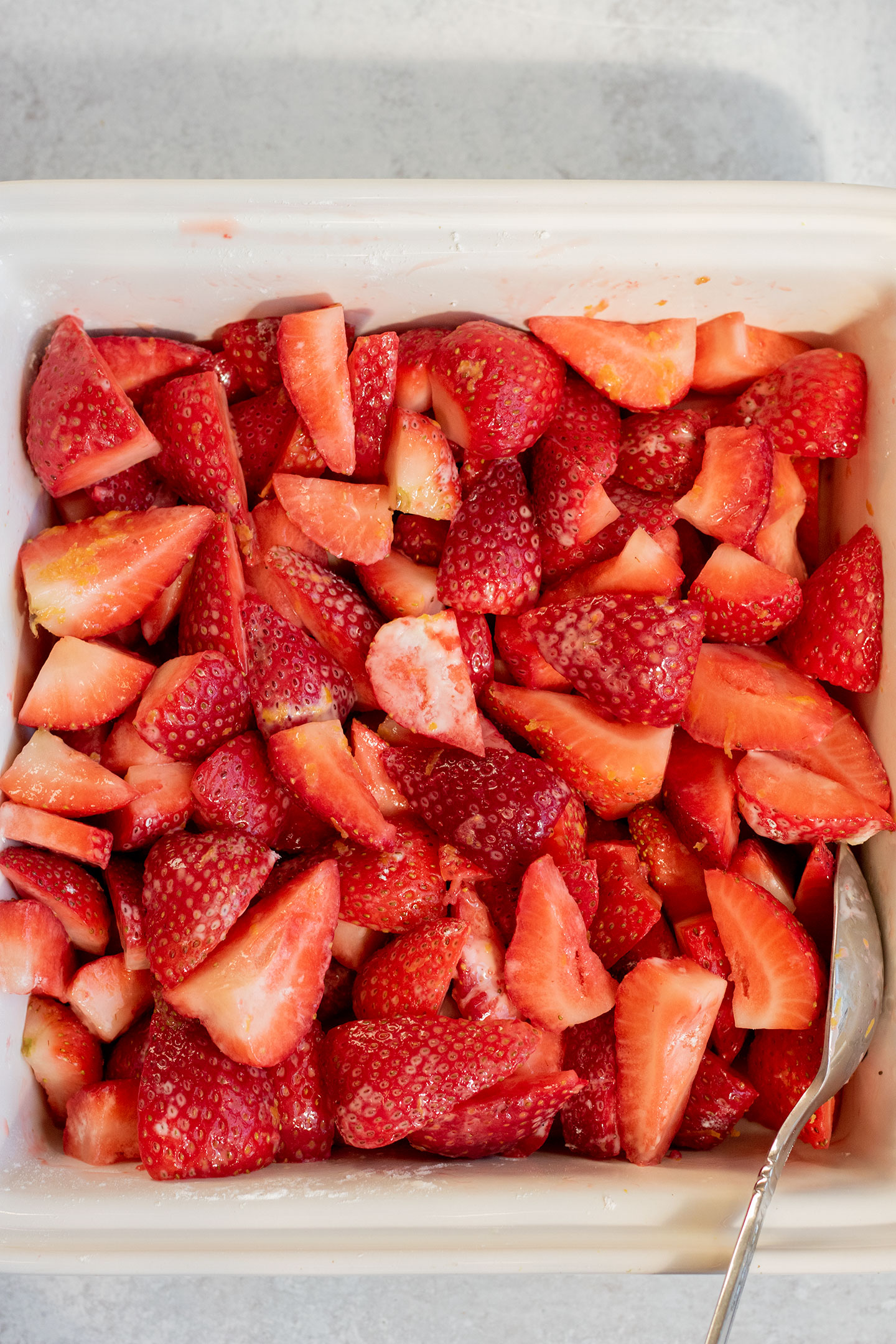 Tossing the strawberries together with lemon and cornstarch in a ceramic baking dish.