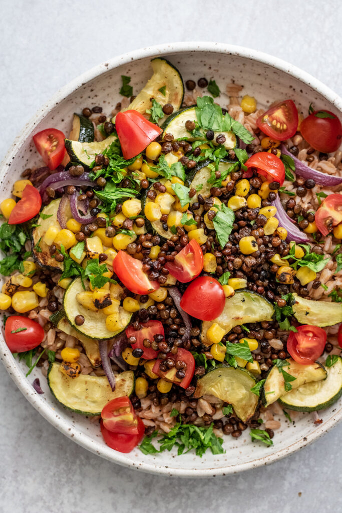 Bowl of farro topped with crispy lentils, tomatoes, zucchini, and onions.