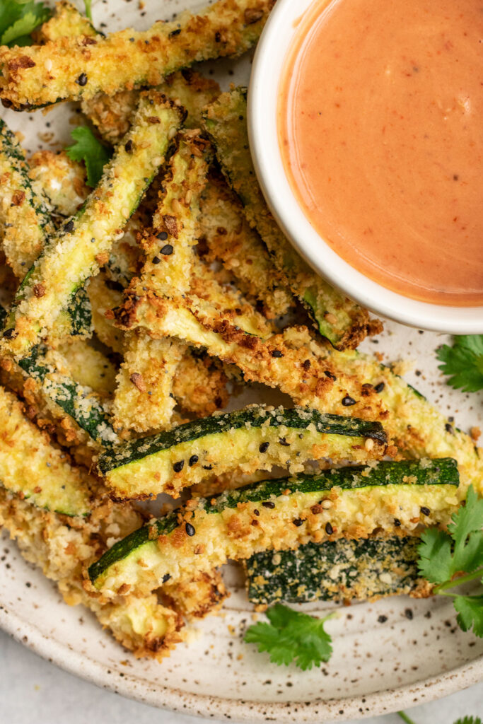 Crispy zucchini fries next to a bowl of dipping sauce.