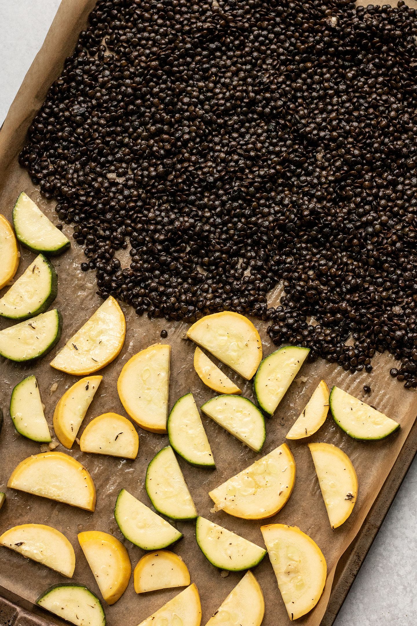 Coated lentils and squash spread out on a parchment paper lined baking tray.