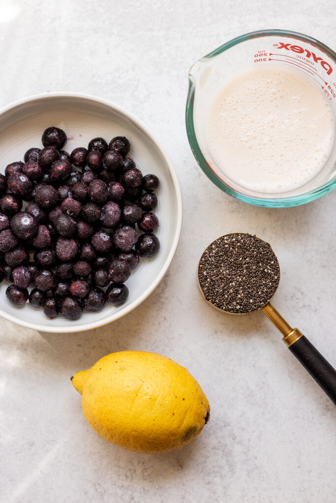 Frozen blueberries, chia seeds, milk and lemon on a kitchen counter.