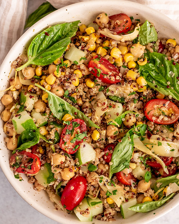 Top down view of a bowl of chickpea quinoa salad tossed together with fresh basil leaves and marinated cherry tomatoes.