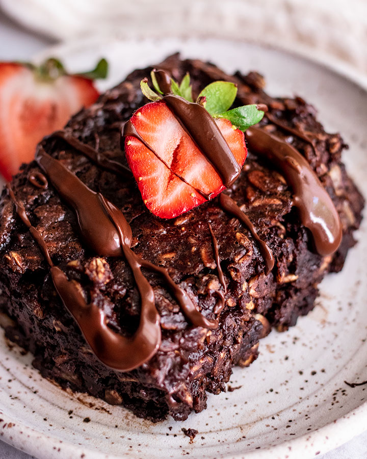 Close up of a slice of chocolate oats after baking in the oven, topped with strawberries and chocolate.