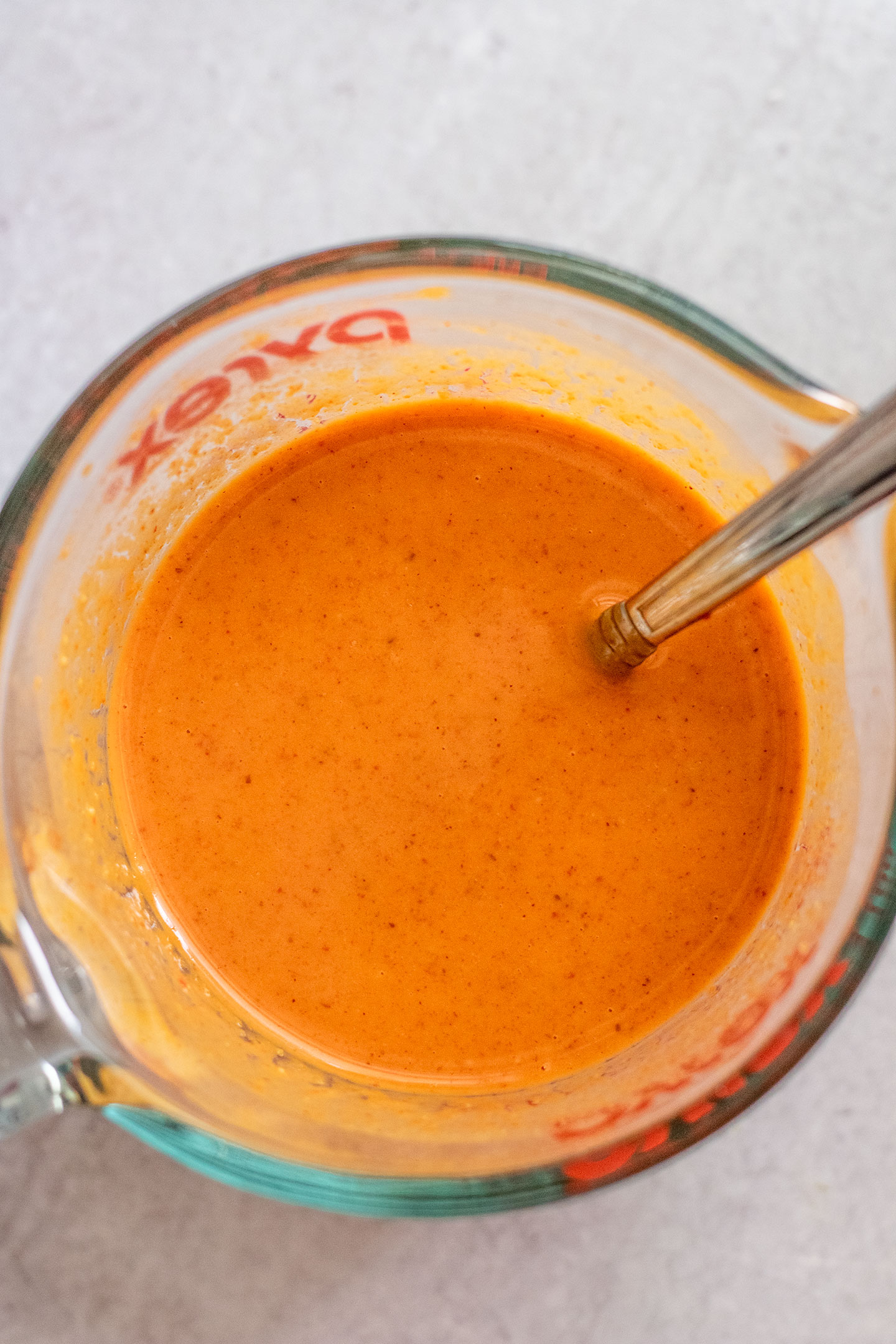 Measuring cup with smooth red curry peanut sauce.