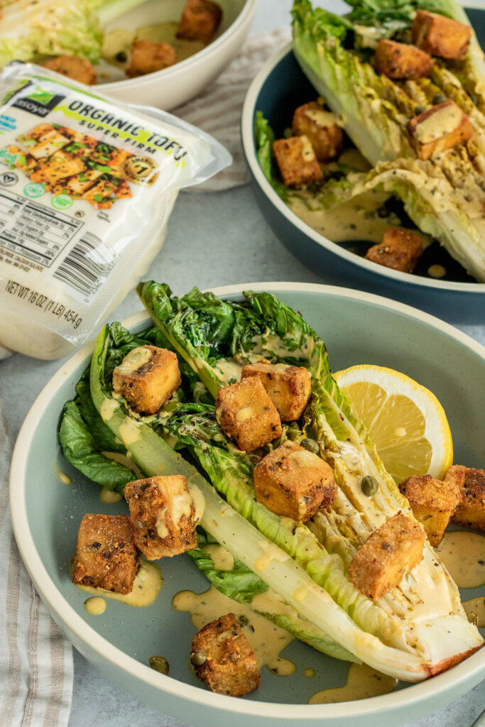 Plated grilled Caesar salad topped with creamy Caesar dressing and crispy tofu croutons.