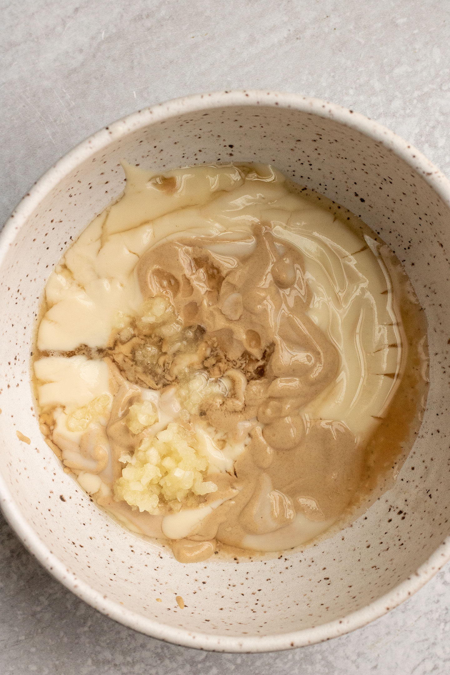 Vegan yogurt, mustard, maple syrup, apple cider vinegar and garlic in a bowl.
